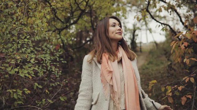 Happy and cheerful woman enjoying autumn, she walking on nature between yellow trees, slow motion