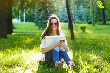 Young woman using cellphone and sitting on the grass on park at sunny day