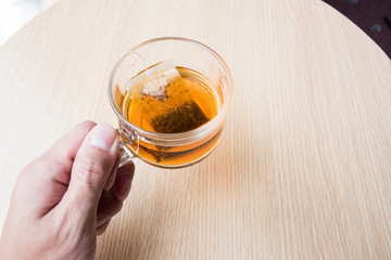 Male hand with cup of hot tea on the wooden table in morning, Top view
