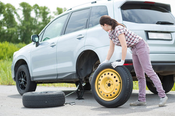 Young european woman changing car tire on rural road