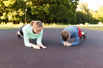 Fitness mother with her 9 years old son. Sports mom with kid doing morning work-out at park. Mum and child do the exercises together, healthy family lifestyle concept