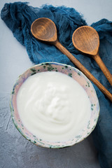 Greek yogurt in a ceramic plate with wooden spoons on a gray concrete background. Selective focus. Rustic style.