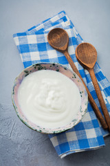 Greek yogurt in a ceramic plate with wooden spoons on a gray concrete background. Selective focus. Rustic style.