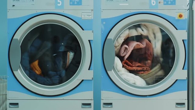 Two large washing machines in public laundry room with rotating drums