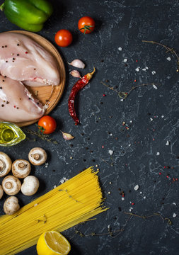 Pasta ingredients. Chicken breasts, Cherry tomatoes, spaghetti pasta and mushrooms on the dark stone table.