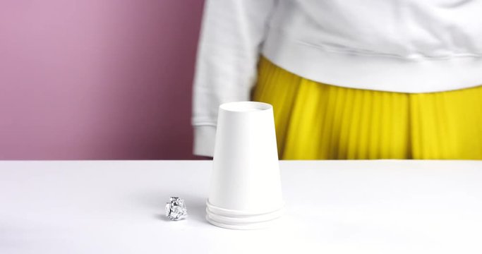 Woman's hands playing with 3 paper cups hiding a ball of foil under one and then switching them around
