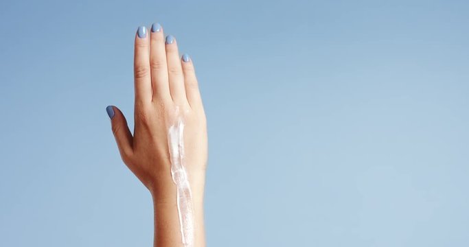 Clean well manicured hands of a young woman, applying hand cream, skin care on light blue background