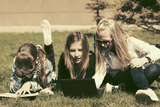 Group of happy teenage school girls lying on a grass in campus