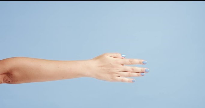 Beautiful young woman's hands with bright blue manicure, one hand gently massaging the other, isolated on light blue background