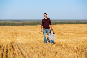Naklejka na ściany i meble Happy father and 2 year old girl walking in the harvested field