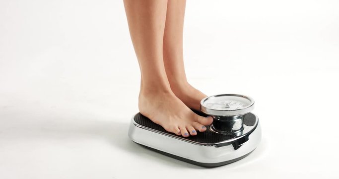 Pretty young woman's feet with blue toenails stepping on an old fashioned black an white scale with round dial isolated on white