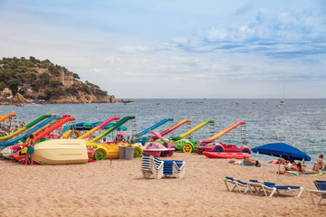 Beach off the coast of Lloret de Mar, Costa Brava. People on the beach in spain lie on sun loungers under umbrellas. Resting under a castle on the beach in Lloret de Mar. Castell de Sant Joan