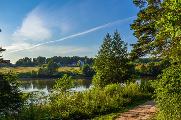 Obraz premium Beautiful rural landscape. Residential house near the river. Trees with bright greenery and blue sky with beautiful clouds. Summer. Russia.