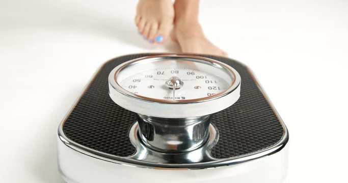 Pretty young woman's feet with blue toenails stepping on an old fashioned black an white scale with round dial isolated on white