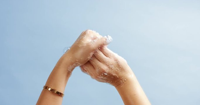 Young attractive woman washing her hands with bubbly soap isolated on light blue background, close up hands only
