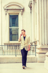 Young American Businessman with little beard working in New York, wearing beige blazer, black pants, shoes, holding laptop computer, walking in business building, talking on cell phone, going to work