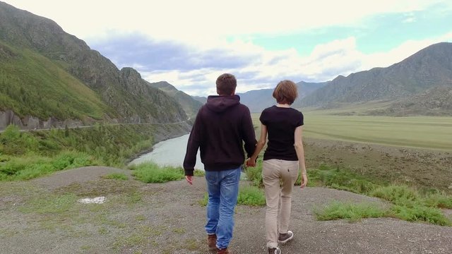 The guy and the girl hold hands and go to the mountain river