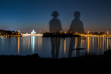 Couple standing holding hands looking at the scenery at night at Suomenlinna island in Helsinki...