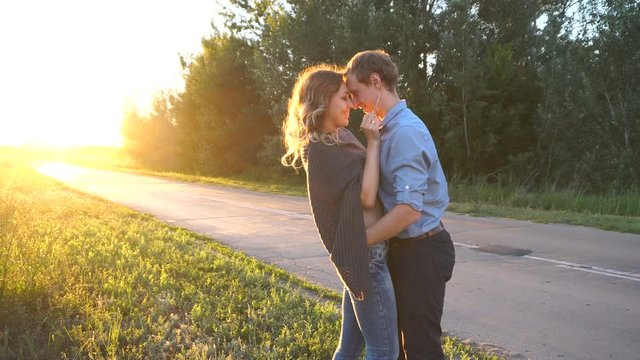 Young loving couple kissing at sunset. They stand in the forest by the road. Road trip.