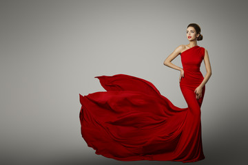 Fashion Model in Red Beauty Dress, Sexy Woman posing evening Gown, Flying Silk Tail over gray background - obrazy, fototapety, plakaty