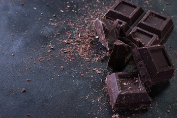Broken chocolate pieces and cocoa powder on dark background