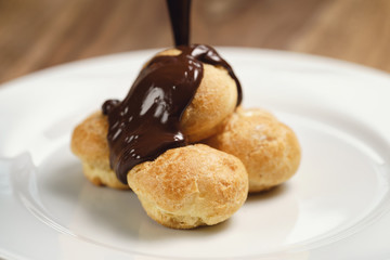 pour chocolate on profiteroles on plate closeup