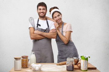 Romantic young couple preparing italian food at home. Picture of charming lady with headband standing in kitchen table and hugging her bearded husband. People, love, relationships, leisure and hobby