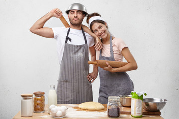 Isolated pciture of beautiful young Caucasian family male and female feeling happy and proud of themselves as they managed to knead dough together for lasagna or pizza, standing at cooking table