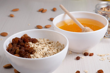 Healthy Breakfast. Oatmeal with raisins in white bowl. Almonds, honey on white  table background