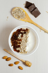 Oatmeal with raisins and yogurt. Oatmeal in the wooden spoon. Almond, chocolate. Flat top view