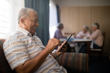 Happy senior man using phone while sitting on sofa