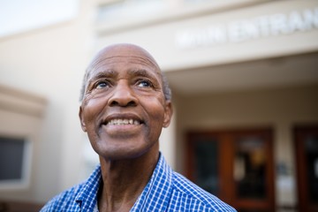 Thoughtful senior man smiling while looking up at nursing home