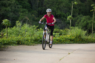 woman cyclist cycling on summer forest trail