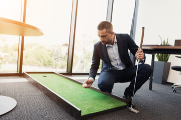 A man in a strict business suit plays in an office in a mini-golf