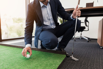 Close up. A man in a business suit plays golf in the office