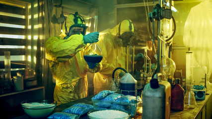 In the Underground Laboratory Two Clandestine Chemists Cook Drugs. They Wear Masks and Coveralls and Work with Beakers and Toxic Chemical Compounds.