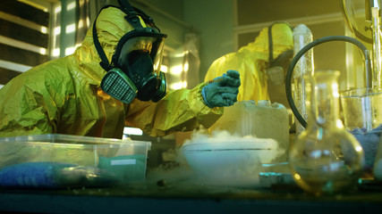 In the Underground Drug Laboratory Two Clandestine Chemists Wearing Protective Masks and Coveralls...