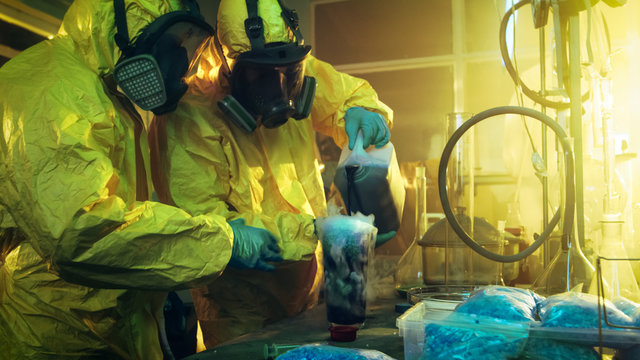 In the Underground Drug Laboratory Two Clandestine Chemists Mix Chemicals while Cooking Narcotics. They Use Canisters and Beakers, Toxic Compounds Create Smoke. They Work in the Abandoned Building.