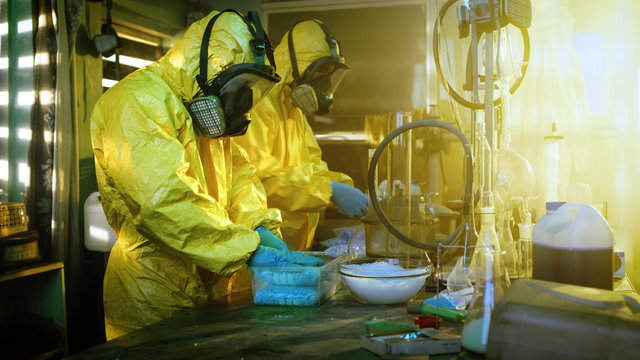 In the Underground Laboratory Two Clandestine Chemists Wearing Protective Masks and Coveralls Pack Bags of Synthesised Crystal Meth into Boxes for Further Distribution.