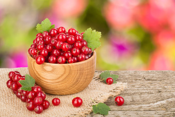 Red currant berries in wooden bowl on wooden table with blurry garden background