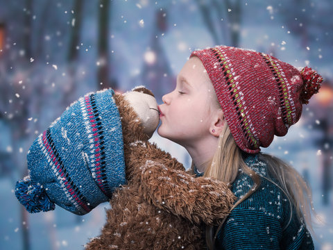 A little girl kisses a Teddy bear. snowing, winter
