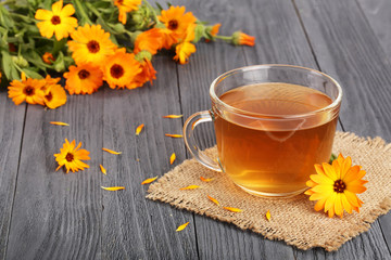 Calendula tea with fresh flowers on black wooden background