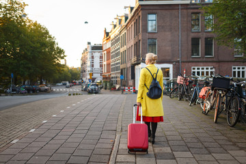 The traveler with suitcase is walking in the street of Amsterdam city in autumn