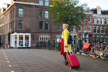 The traveler with suitcase is walking in the street of Amsterdam city in autumn