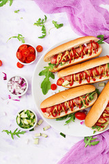 Hot dog with sausage. bacon, cucumber, tomato and red onion on white plate. Top view. Flat lay.