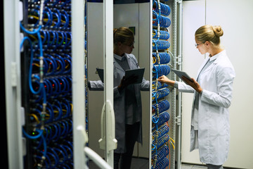 Portrait of young woman wearing lab coat working with servers in supercomputer research center, copy space