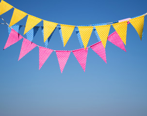Fototapeta premium garlands with multi-colored flags against a background of blue sky. garland of pink, blue and yellow flags. festive background. Party flags decoration on outdoor.