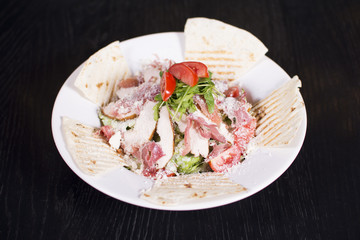 Salad with prosciutto and cheese on white plate close up. Served restaurant table. Delicious meal at a luxury restaurant.