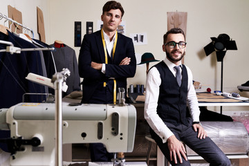 Portrait of two  handsome young tailors posing, looking at camera in traditional atelier studio...