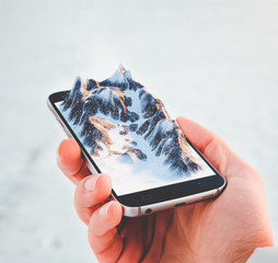 Man holding smartphone with mountains on the screen.